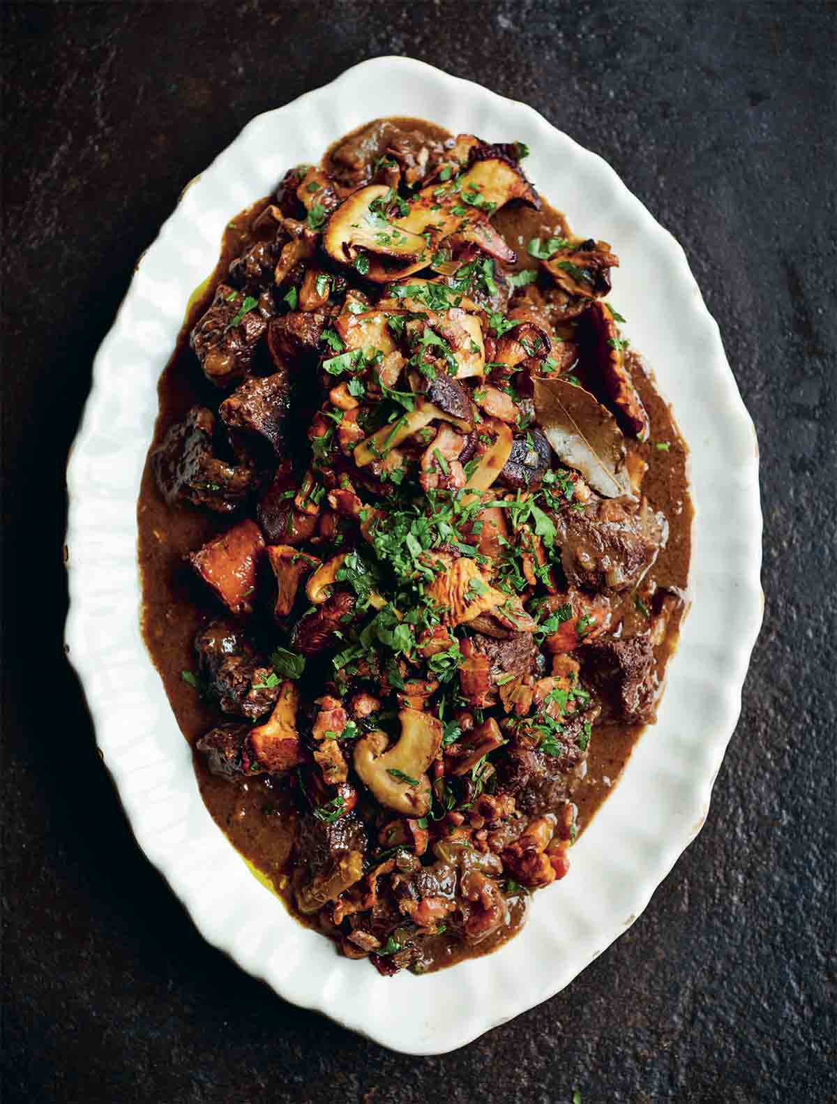 A white platter with beef Bourguignon, filled with beef, carrots, and mushrooms