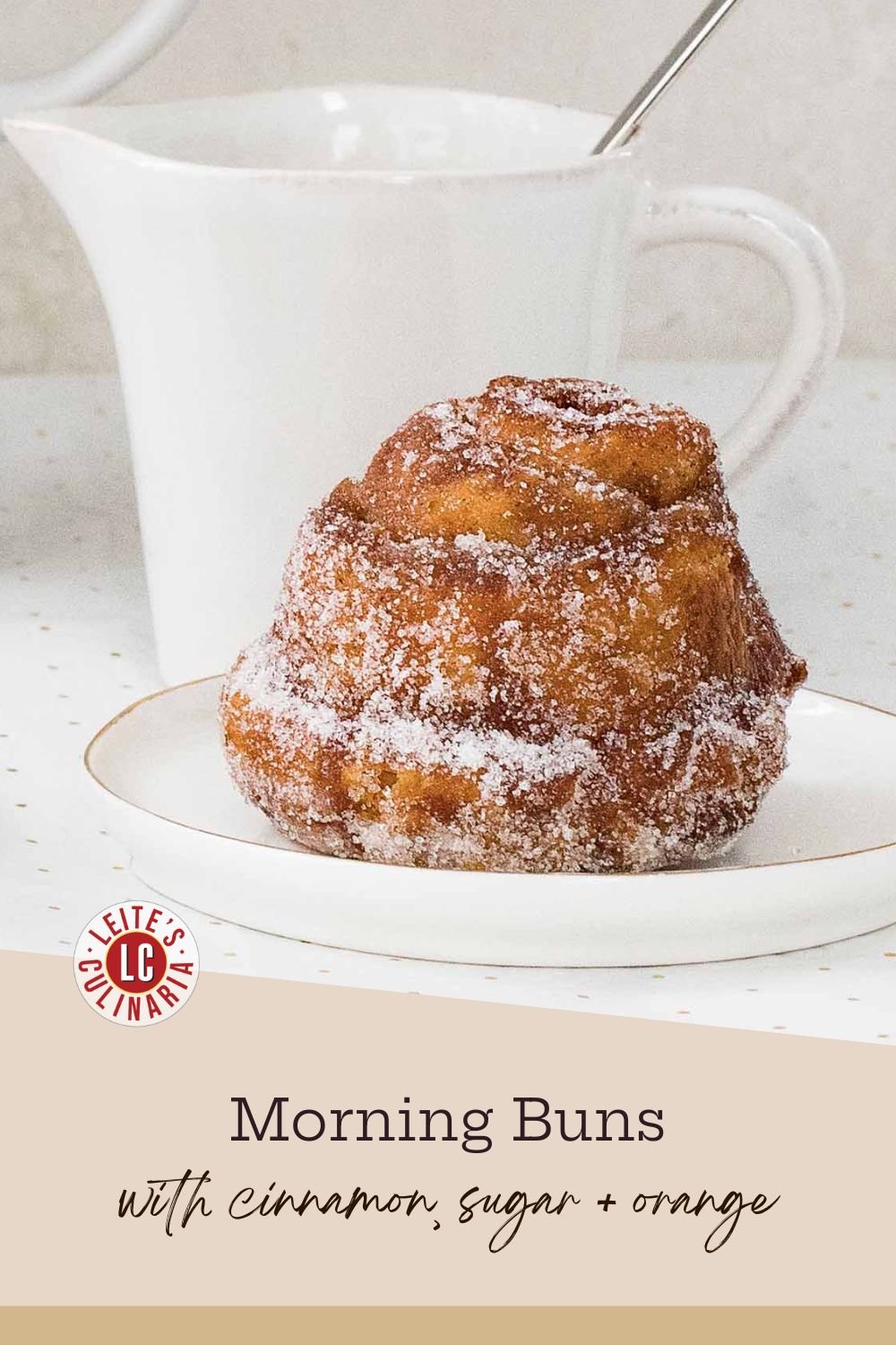 A fluffy, sugar-coated morning bun sits on a small white plate with a gold rim.