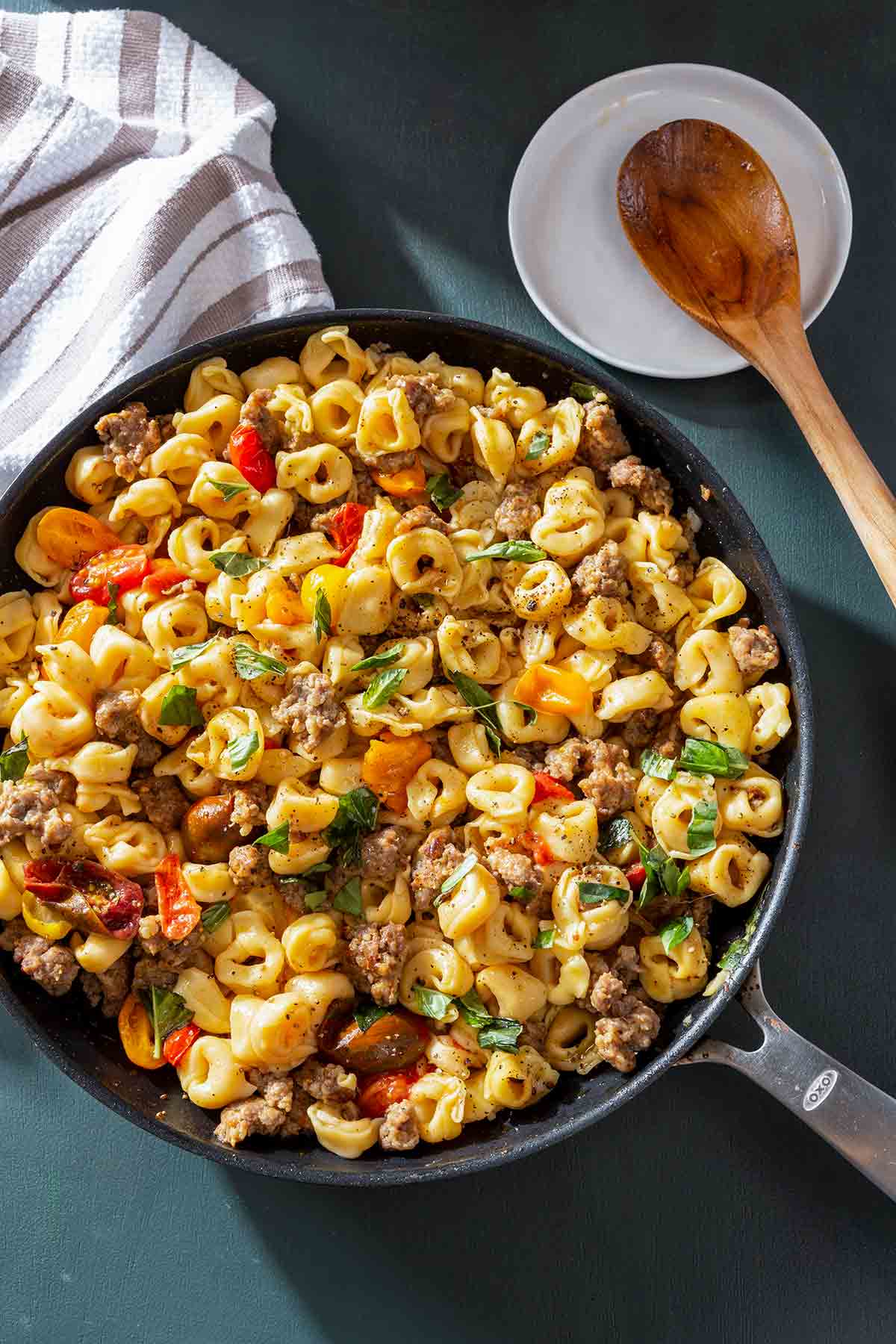 A pan of skillet tortellini with sausage and cherry tomatoes sprinkled with chopped basil