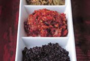 A tapenade trio, black olive, sun-dried tomato, and green olive, in a triple white serving dish.