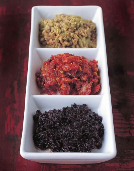 A tapenade trio, black olive, sun-dried tomato, and green olive, in a triple white serving dish.
