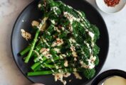 A black plate with broccolini with tahini sauce.