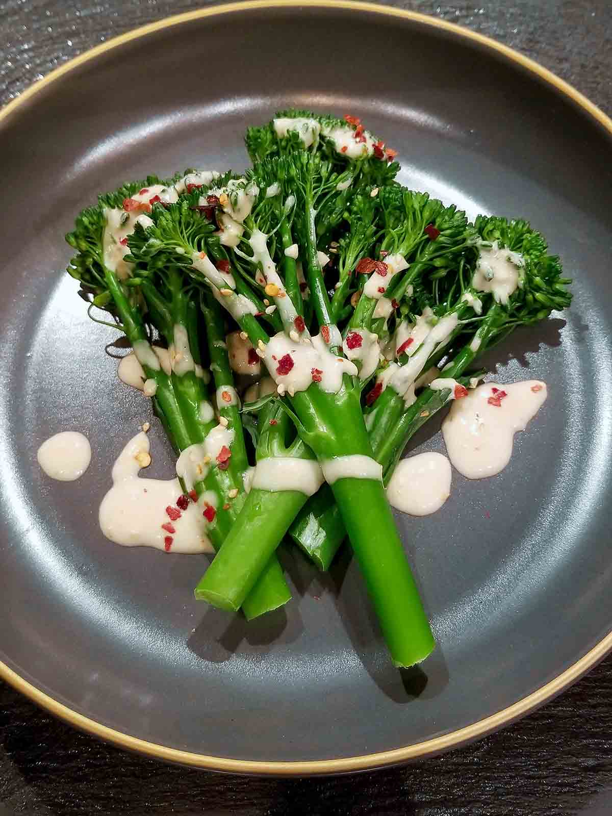 A gray plate with broccolini with tahini sauce
