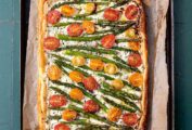 A cherry tomato, asparagus, and herbed ricotta tart on parchment on a baking sheet