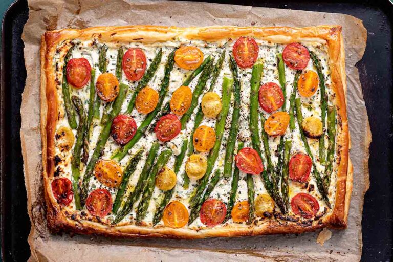 A cherry tomato, asparagus, and herbed ricotta tart on parchment on a baking sheet