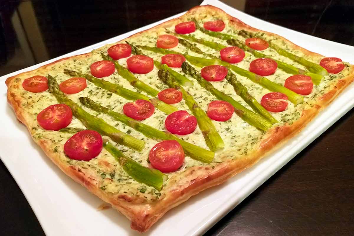 A cherry tomato, asparagus, and herbed ricotta tart on a white serving platter.