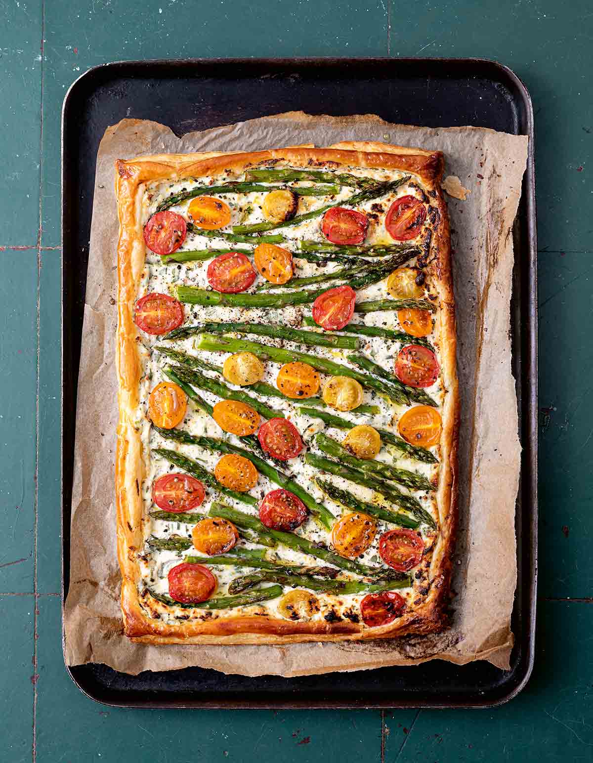 A cherry tomato, asparagus, and herbed ricotta tart on parchment on a baking sheet