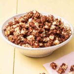 A bowl of chocolate-covered popcorn on a yellow background