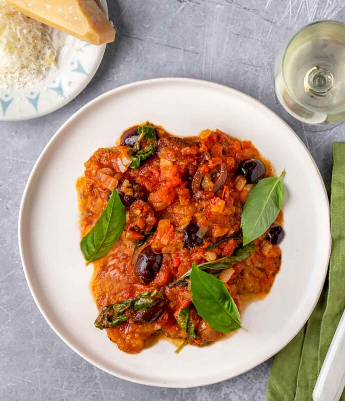A plate of classic chicken cacciatore topped with basil leaves and a glass of wine on the side.