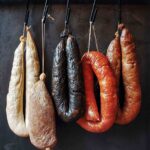 Five links of common Portuguese sausages, including homemade chouriço, hanging from hooks on a wooden dowel