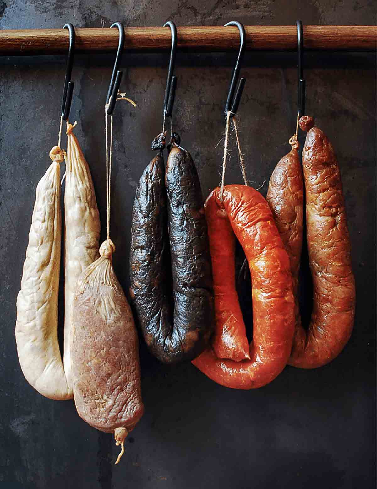 Five links of common Portuguese sausages, including homemade chouriço, hanging from hooks on a wooden dowel