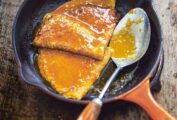A small orange skillet with two crêpes Suzette and a spoon topped with citrus sauce.