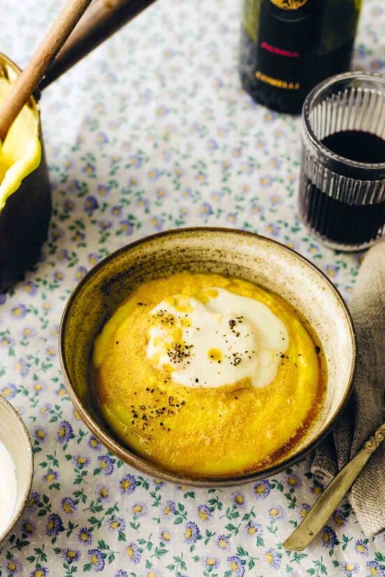 An earthenware bowl filled with Friulian polenta and topped with cheese sauce and black pepper.