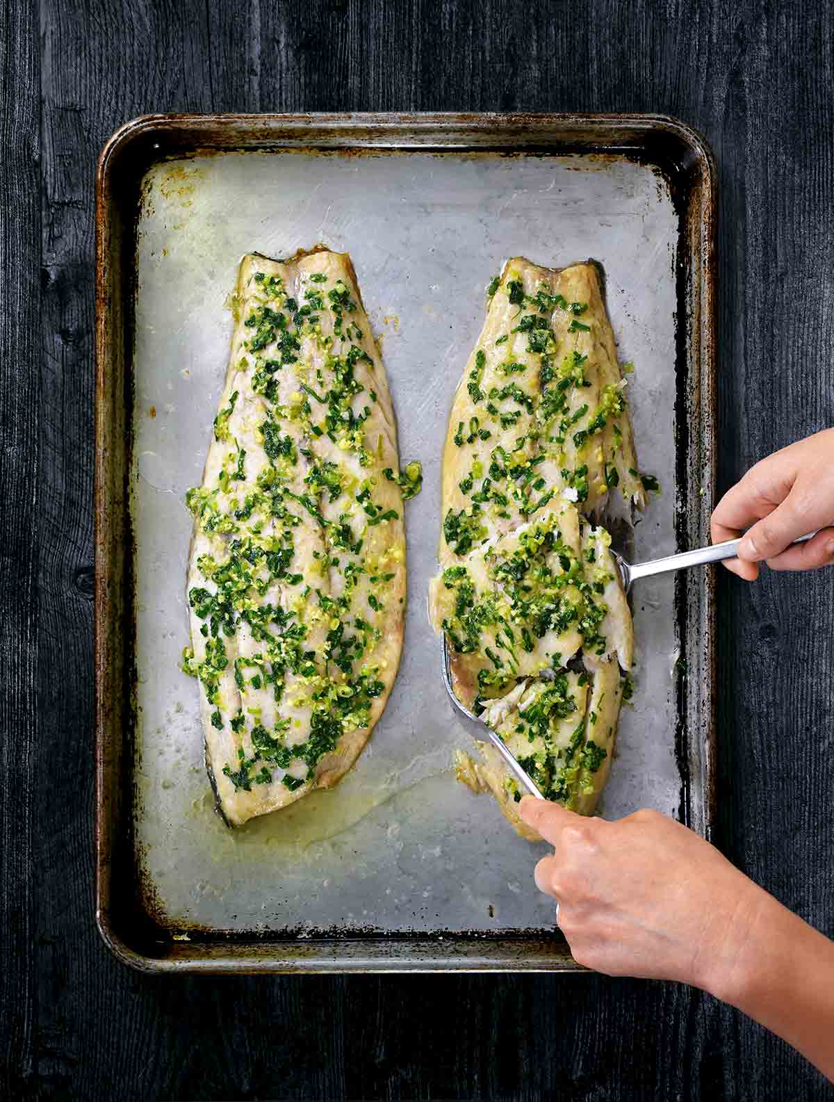 a woman's hands lifting ginger-scallion fish fillets from a baking sheet