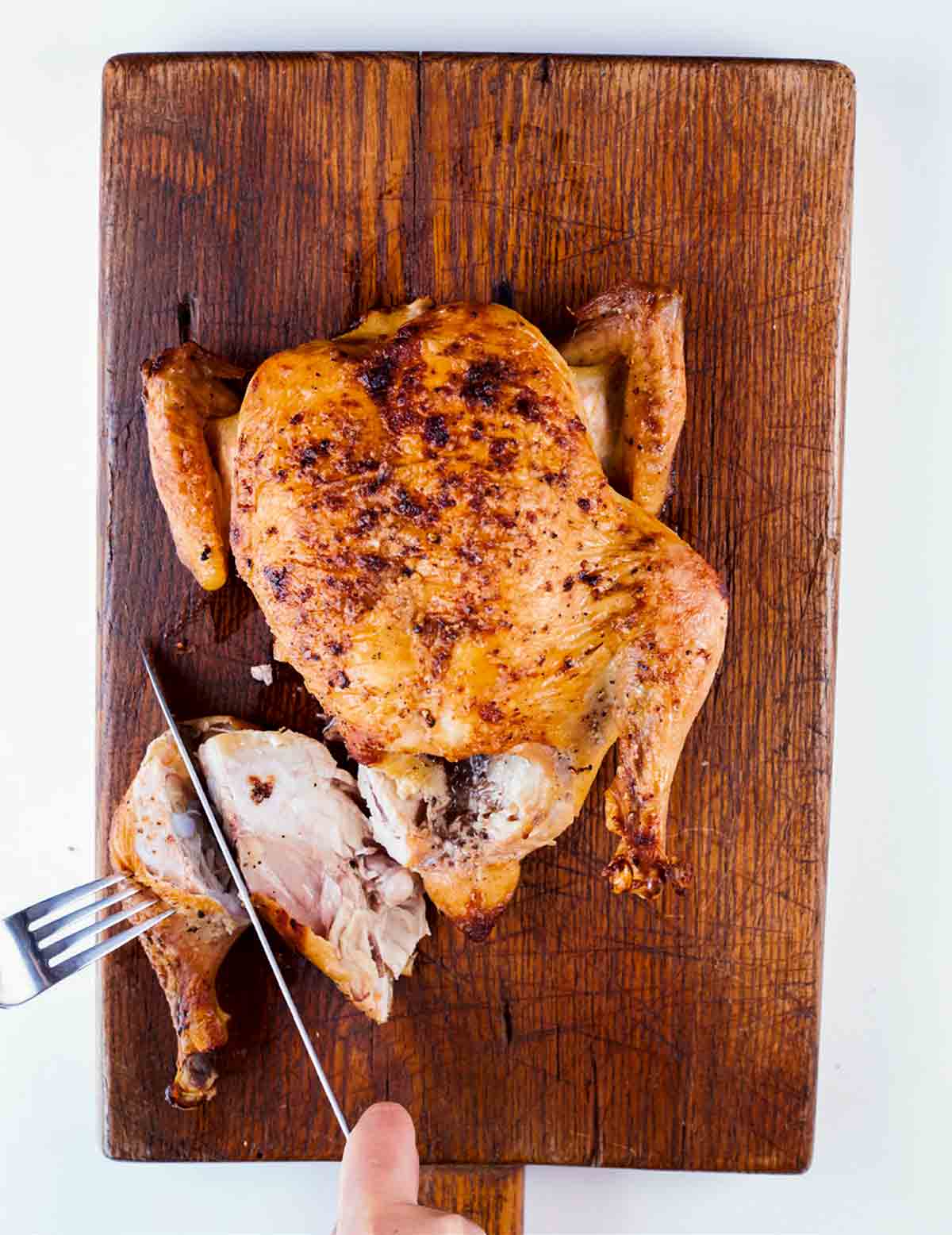 A person carving a roast chicken on a cutting board.