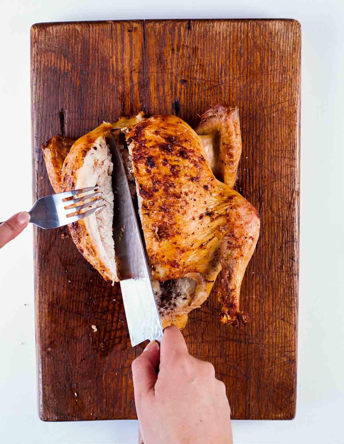 A person carving a roast chicken on a cutting board.