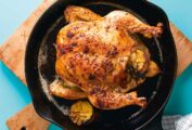 A roast chicken stuffed with lemon in a cast iron skillet on a wooden cutting board.