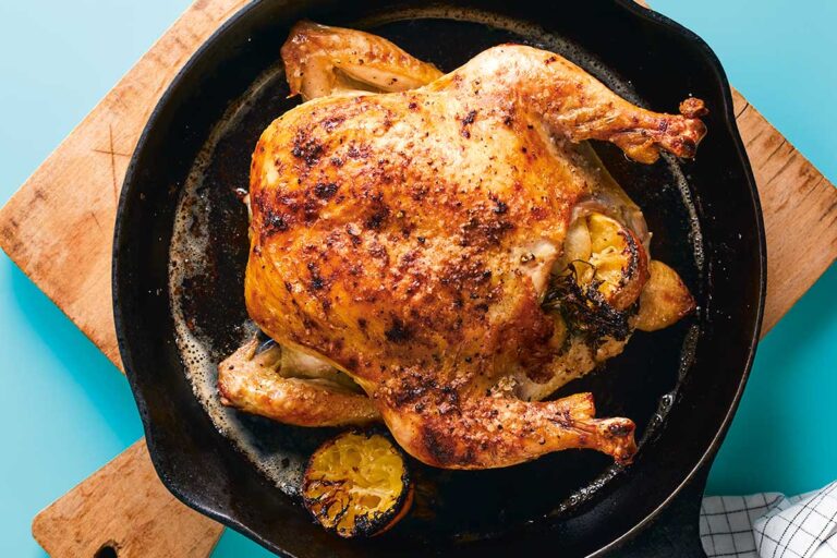 A roast chicken stuffed with lemon in a cast iron skillet on a wooden cutting board.