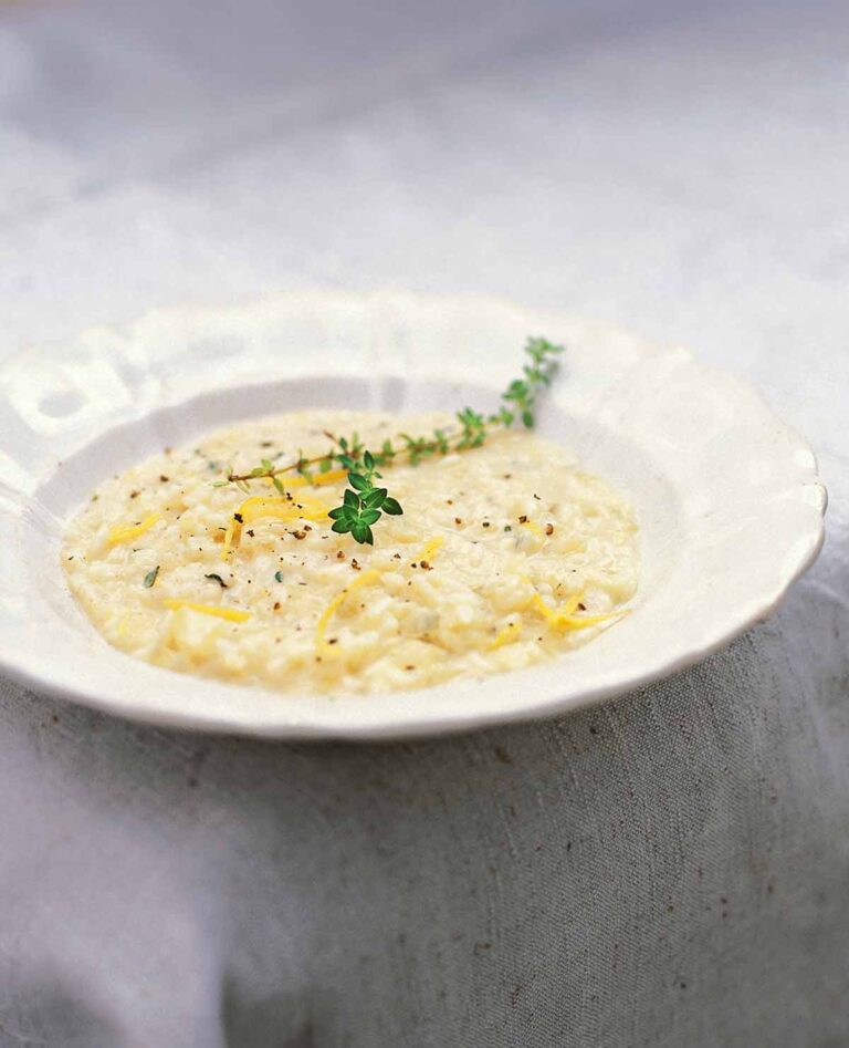 A white bowl filled with lemon and thyme risotto and topped with a sprig of thyme and some lemon zest