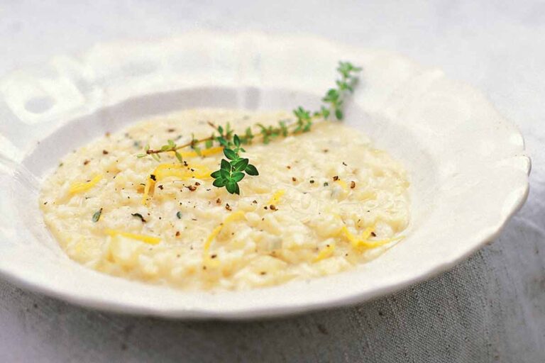 A white bowl filled with lemon and thyme risotto and topped with a sprig of thyme and some lemon zest