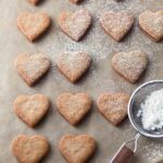Fifteen Linzer heart cookies being dusted with confectioners' sugar