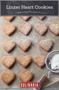 Fifteen Linzer heart cookies being dusted with confectioners' sugar