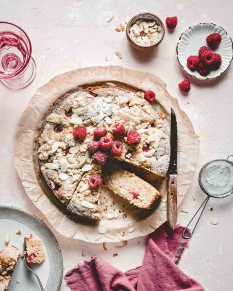 A raspberry almond crumble cake, with a slice on its side on a circle of parchment paper