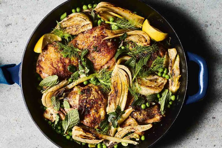 A cast-iron skillet filled with chicken thighs, peas, and fennel.