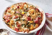 Spaghetti primavera pie in a large dish--spaghetti topped with zucchini, tomatoes, onions, Parmesan and mozzarella cheese.