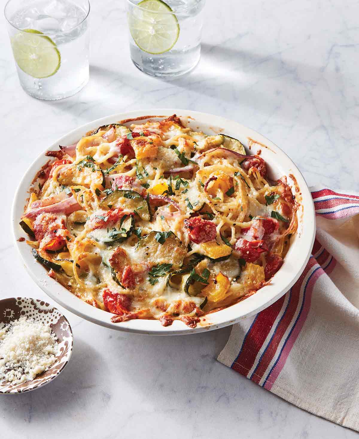 Spaghetti primavera pie in a large dish--spaghetti topped with zucchini, tomatoes, onions, Parmesan and mozzarella cheese.