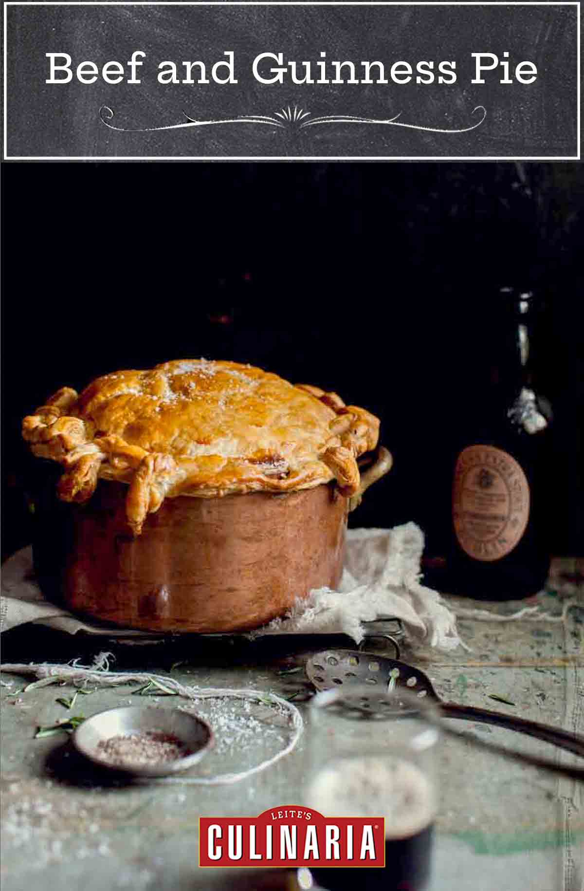 A copper pot filled with beef and Guinness pie topped with puff pastry on a towel on a cooking rack with a bottle behind it.