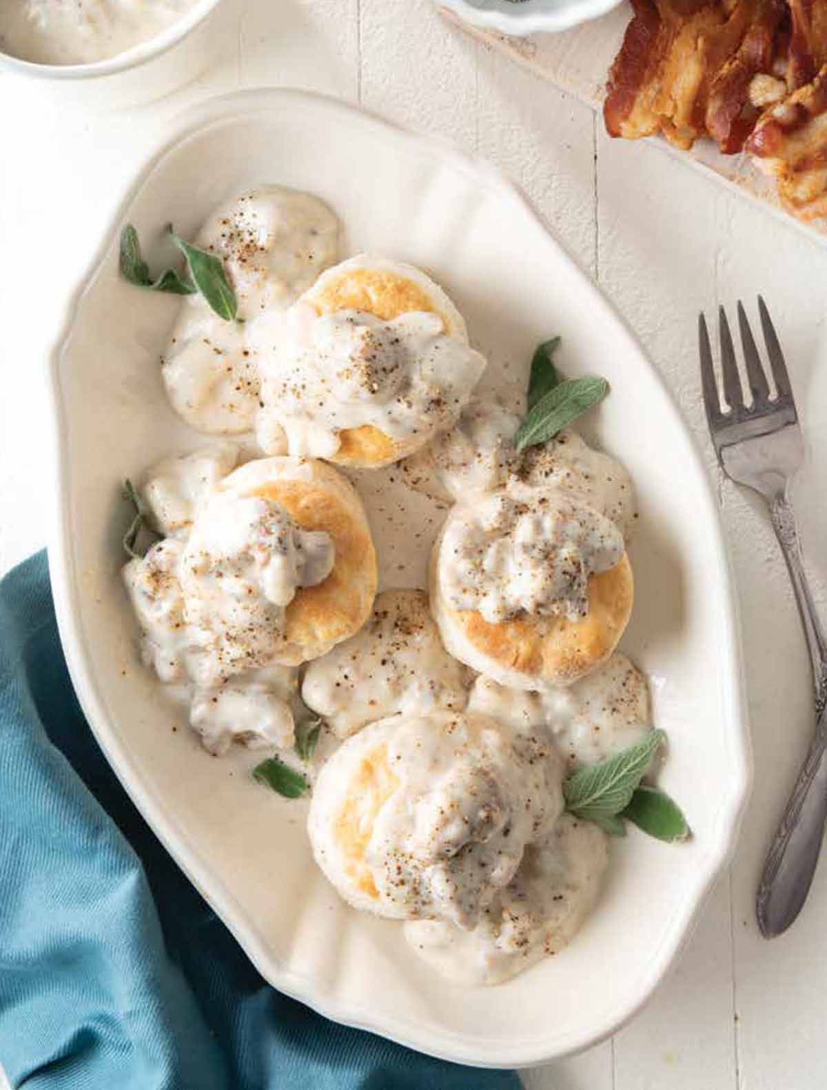 A serving platter with four cat head biscuits and gravy and sage leaves to garnish.