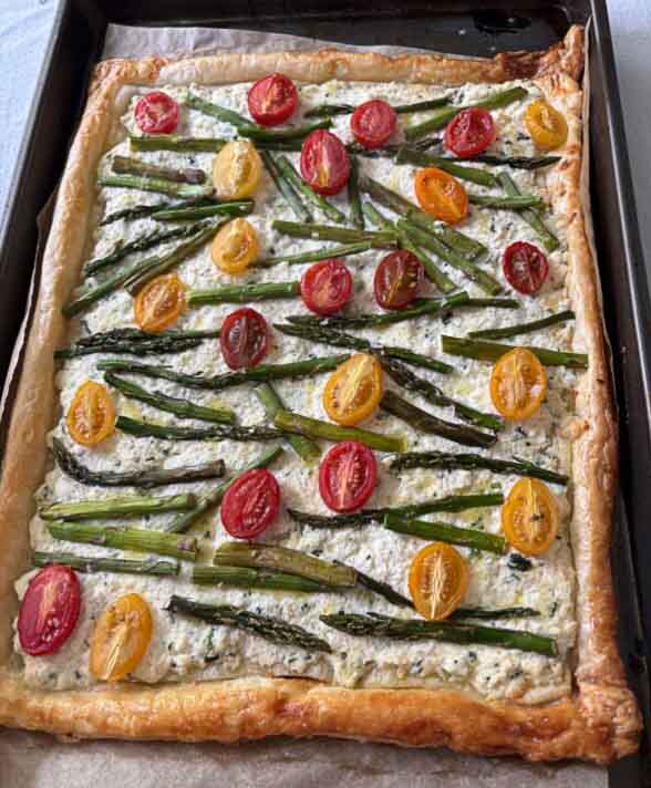A puff-pastry tart filled with halved cherry tomatoes, asparagus spears, and ricotta cheese.
