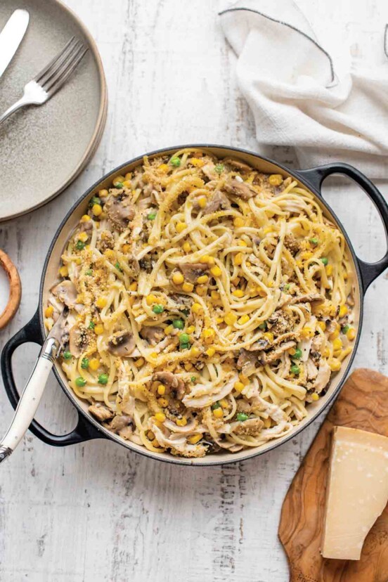A dutch oven filled with chicken, mushroom, and corn tetrazzini on a white wooden table.