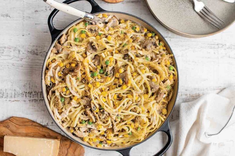 A dutch oven filled with chicken, mushroom, and corn tetrazzini on a white wooden table.