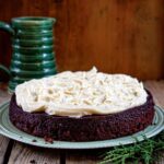 En choklad stout tårta toppad med brunt smör cream cheese frosting på en grön tallrik med en grön mugg i bakgrunden.