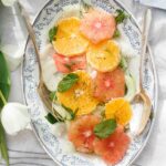 A citrus fennel salad assembled on a white and blue serving platter, topped with fresh herbs.