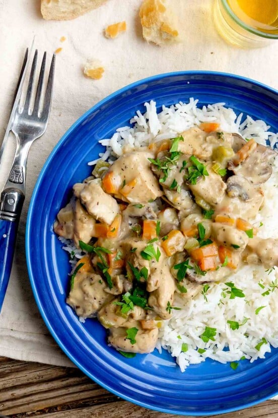 A blue plate with a serving of creamy French chicken stew served over rice and garnished with parsley.