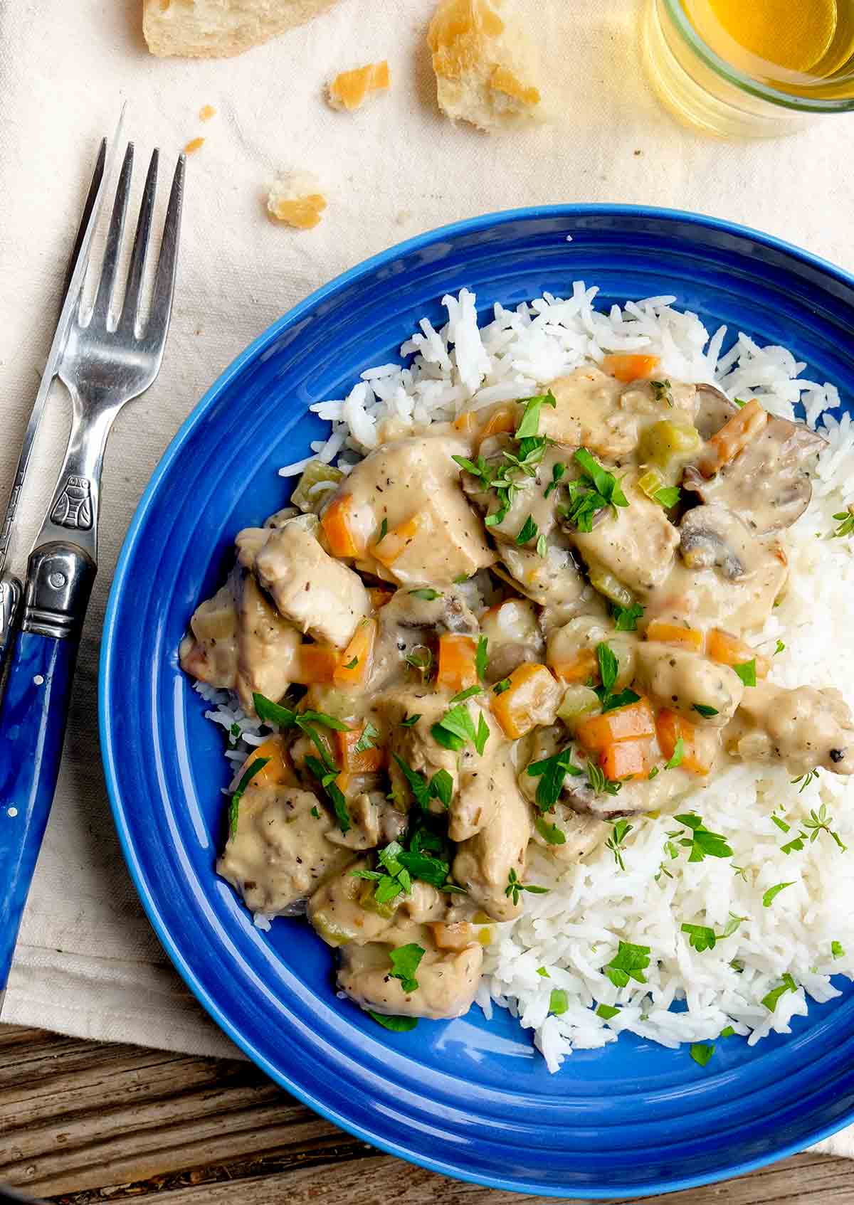 A blue plate with a serving of creamy French chicken stew served over rice and garnished with parsley.