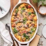 An oval casserole dish filled with easy breakfast strata on a wooden board with a wedge of Parmesan and a spoon on the side.