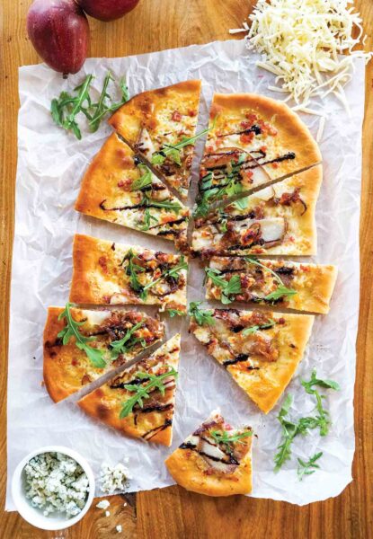 An oval flatbread with pancetta, pear, and blue cheese, cut into 10 wedges.