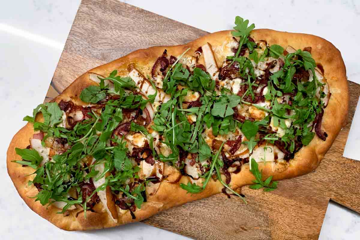 A whole flatbread with pancetta, pear, and blue cheese on a wooden serving board.