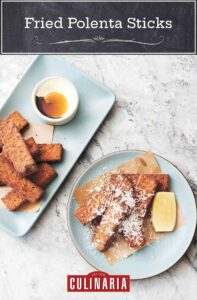Four fried polenta sticks on a plate topped with Parmesan and a lemon wedge on the side.