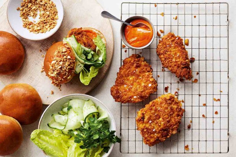 Three pieces of Gordon Ramsay's cornflake chicken on a cooking rack with buns, salad, and peanut topping on the side.