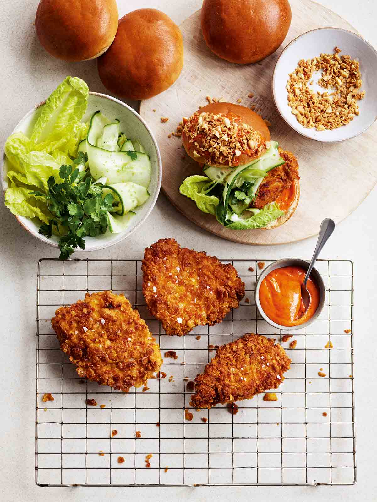 Three pieces of Gordon Ramsay's cornflake chicken on a cooking rack with buns, salad, and peanut topping on the side.