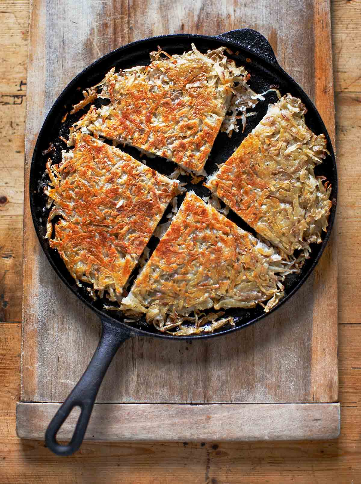 Cast iron skillet with a pan boxty (Irish potato pancakes) in it, on a wooden cutting board