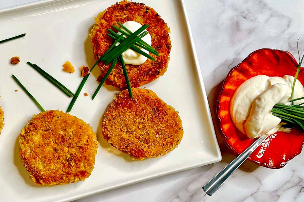 Three sweet potato patties on a platter with a bowl of creme fraiche on the side.