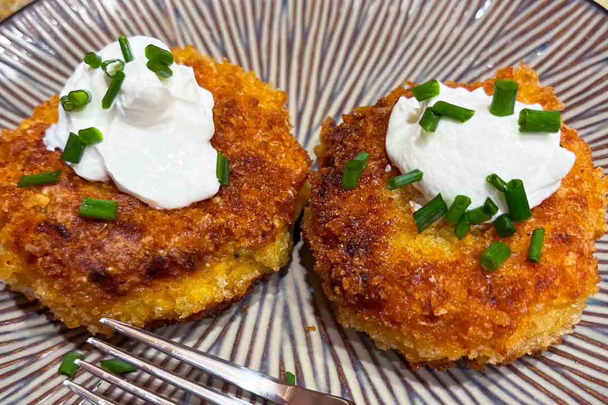 Two sweet potato patties on a striped plate, topped with sour cream and chives.