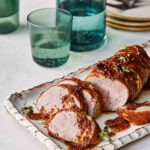 A sliced air fryer prosciutto-wrapped pork tenderloin covered in mustard-fig sauce on a white platter