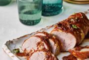 A sliced air fryer prosciutto-wrapped pork tenderloin covered in mustard-fig sauce on a white platter
